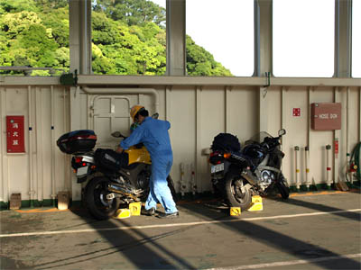 三和商船フェリー「第二天長丸」の車両甲板の壁際に駐車したバイクと甲板を清掃している船員