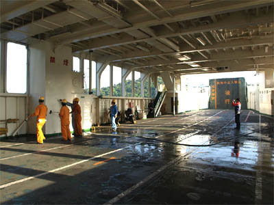三和商船フェリー「第二天長丸」の車両甲板の壁際に駐車したバイクと甲板を清掃している船員