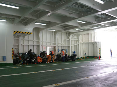 津軽海峡フェリー「大函丸」の車両甲板の壁際にバイクを駐車したバイクを固定している甲板作業員