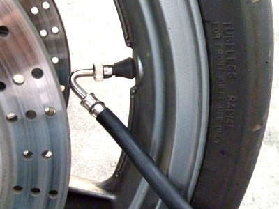 Un inflador de gasolinera conectado a un neumático delantero de motocicleta usando una manguera de carga de aire