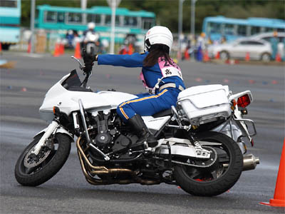 ヘルメットから飛び出たロングヘアーをなびかせて走る女性白バイ隊員とバイク(CB1300)