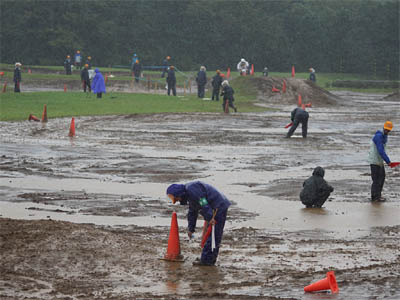 大雨の中をパイロンの設置場所に目印の石灰を撒く全国白バイ安全運転競技大会の審判員