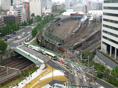 国道15号線の八山橋交差点と京浜急行の開かずの踏切で待つ車とバス、陸橋の下を走行するJRの山手線と東海道線の車両