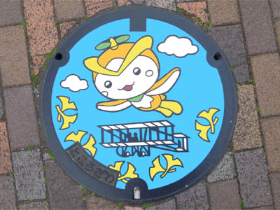 所沢市のデザインマンホール（カラーマンホール）で所沢市のマスコットキャラクター「トコろん」と航空発祥の地、所沢のシンボル的な飛行機「アンリ・ファルマン号」が描かれている
